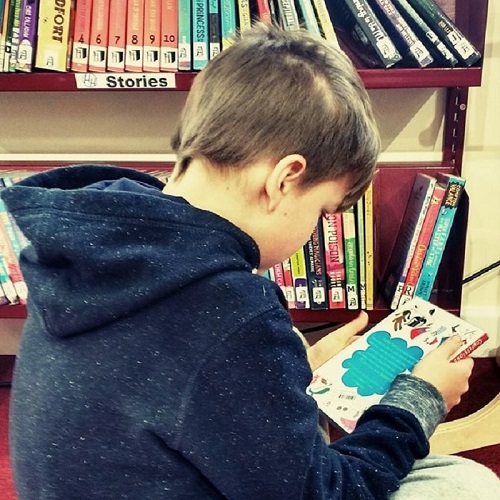 A young boy reads a book at the community library.